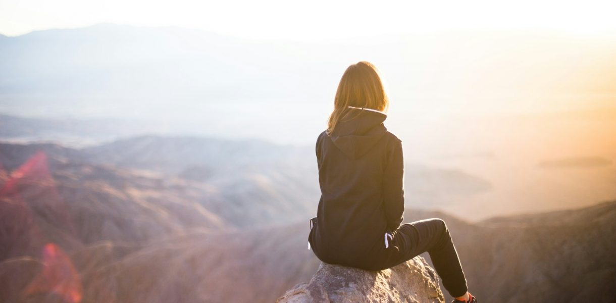 person sitting on top of gray rock overlooking mountain during daytime