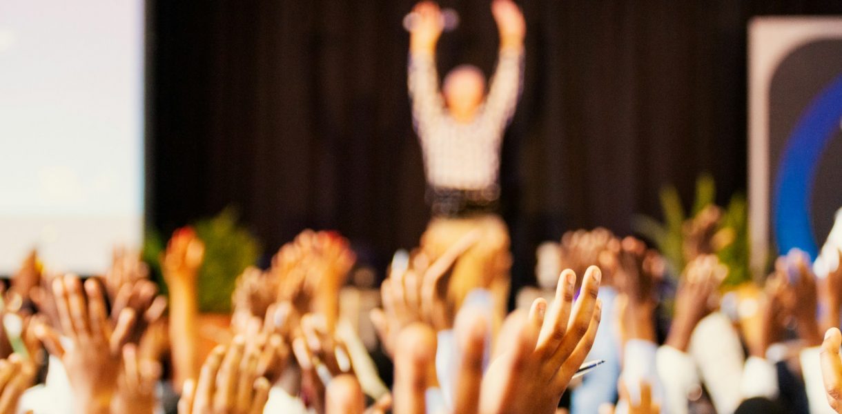 people raising hands with bokeh lights conférence